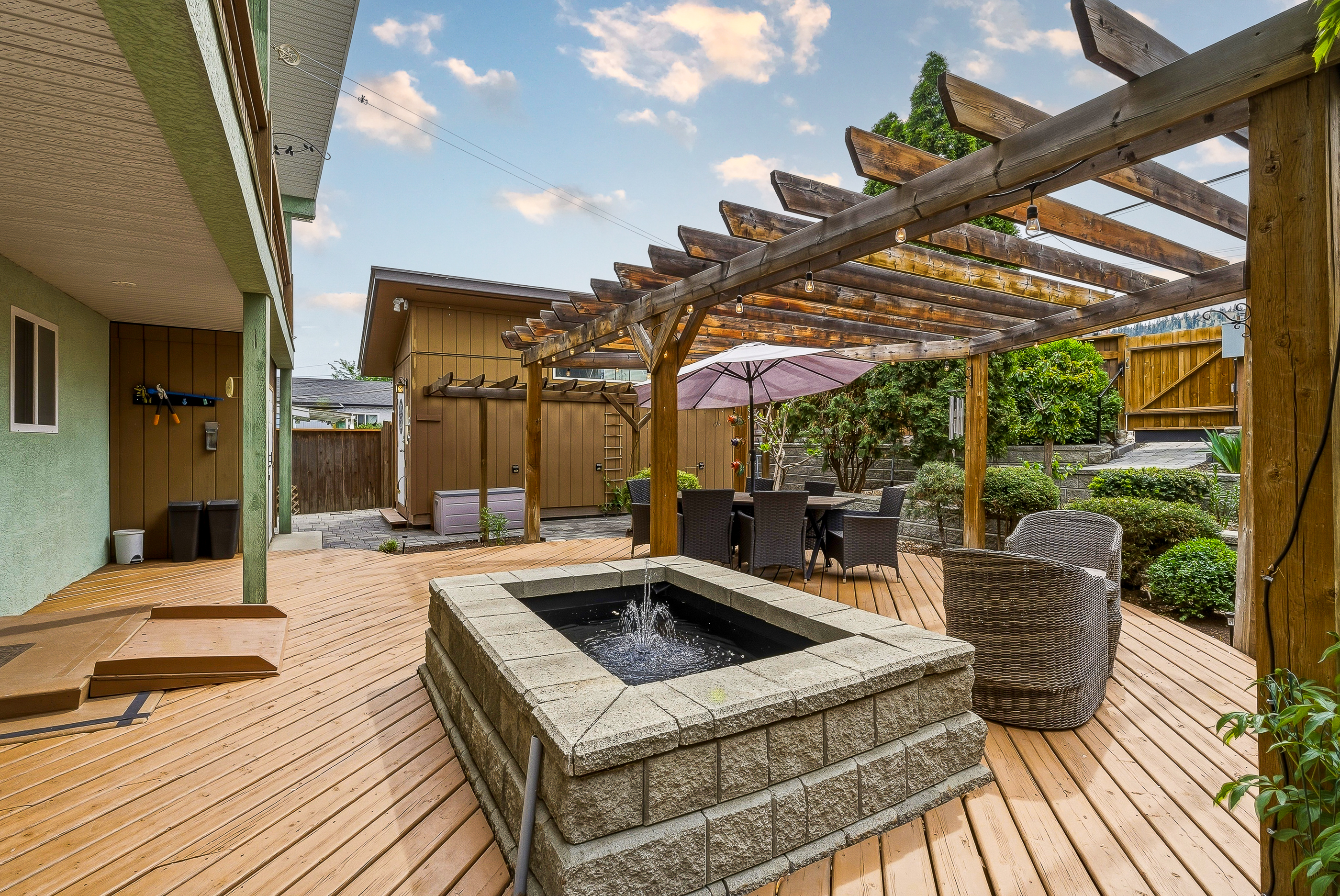 Stone water feature on the back deck at 1127 Columbia St, pergola overhead, outdoor dining set, lounge chairs and lush plantings