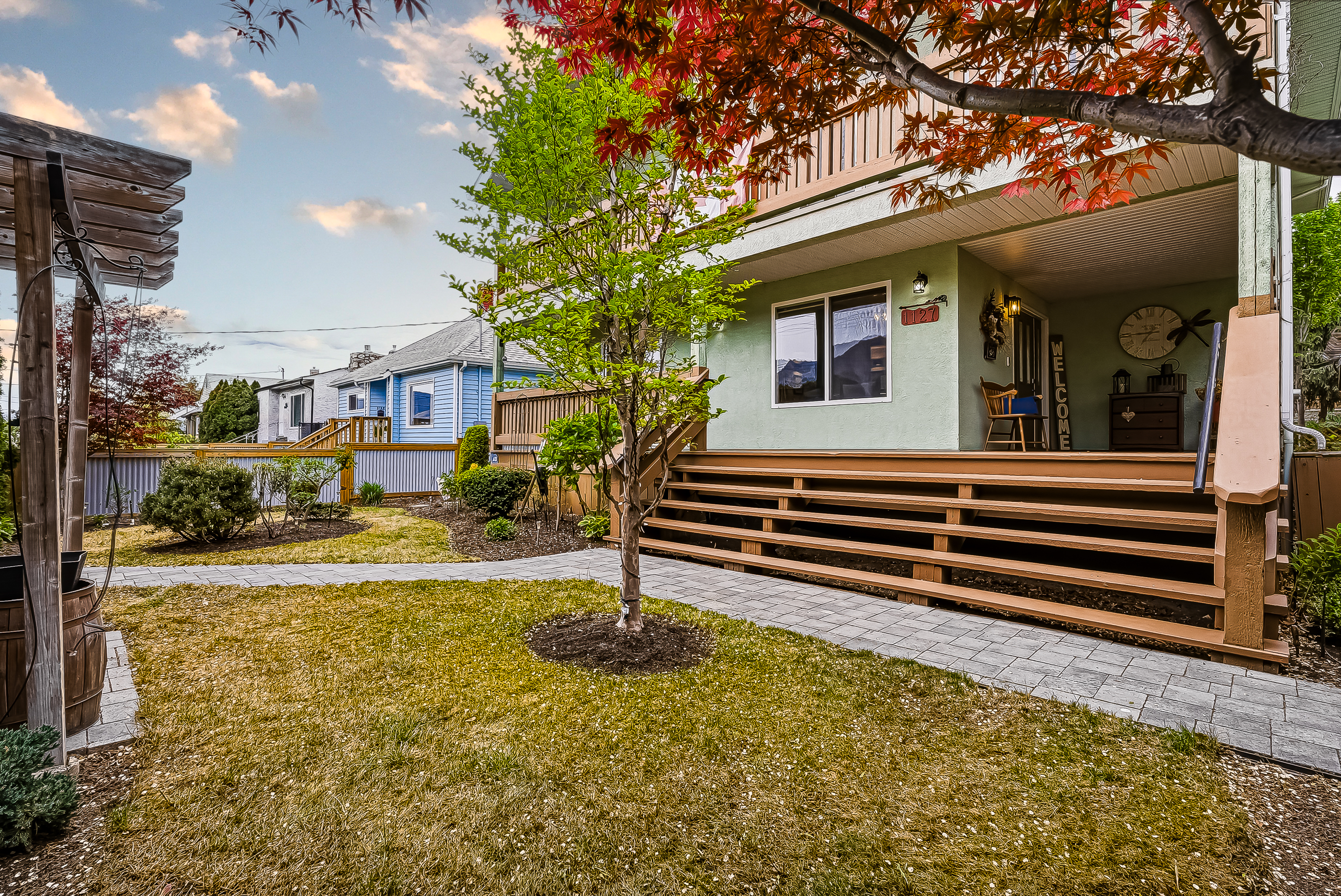 Side view of the front yard with paver path, ornamental maple, lawn and the lower veranda of the home in the background