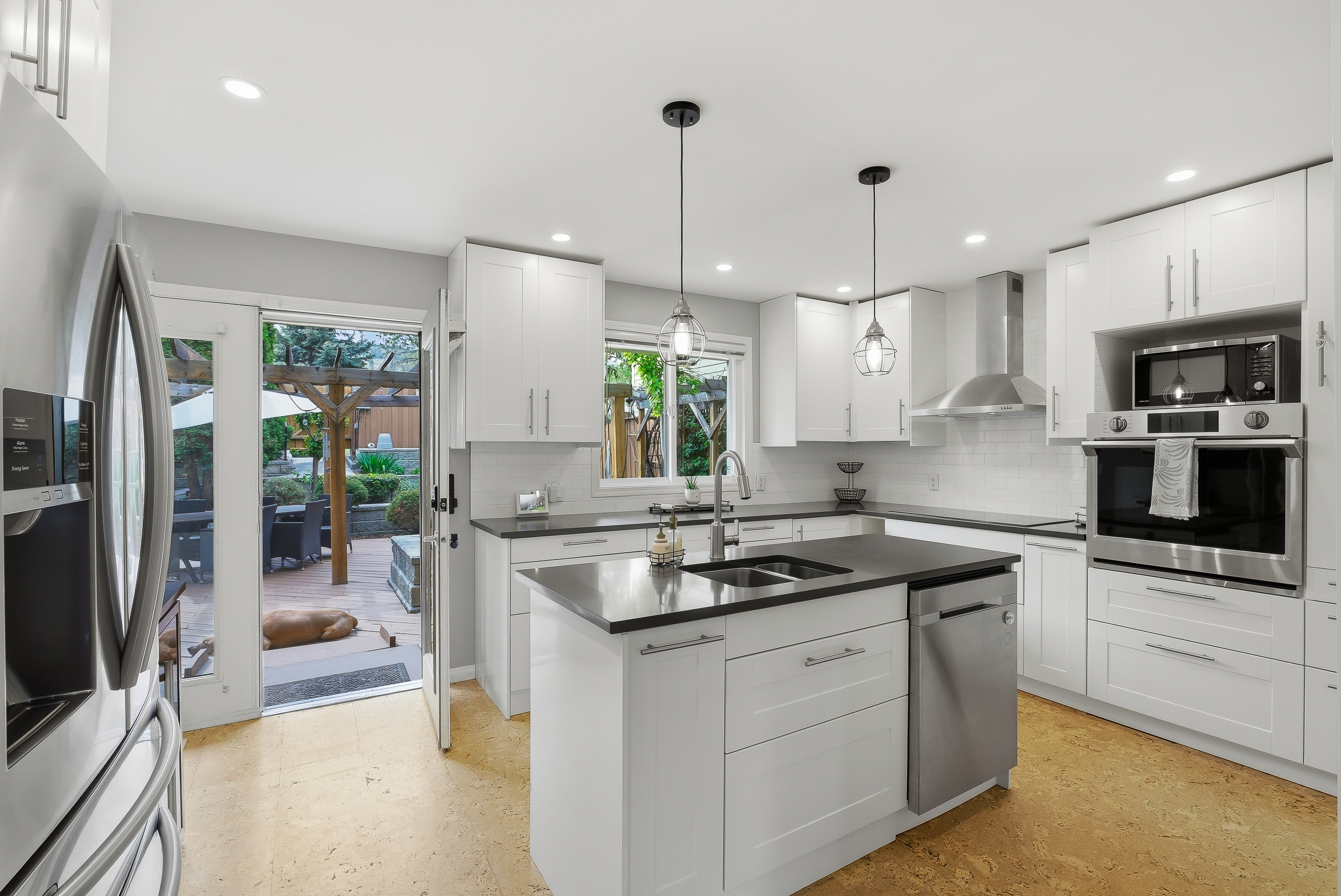 White shaker kitchen at 1127 Columbia St with dark quartz island, beautiful pendant lights, smart stainless appliances, wall oven, glass cooktop and a door to the back deck