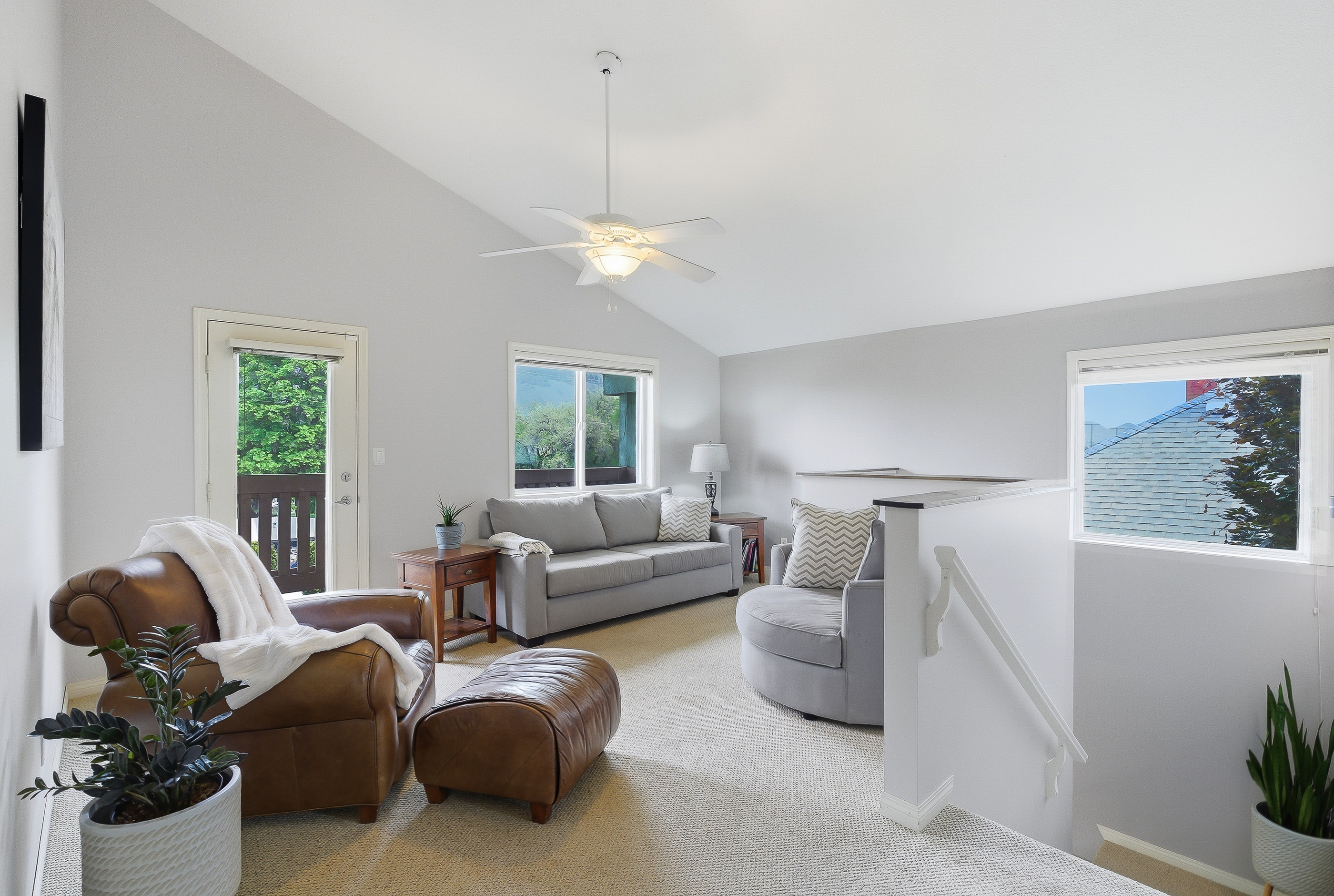 Upstairs sitting area with vaulted ceiling, walk-out balcony door, leather chair and loveseat at the top of the stairs