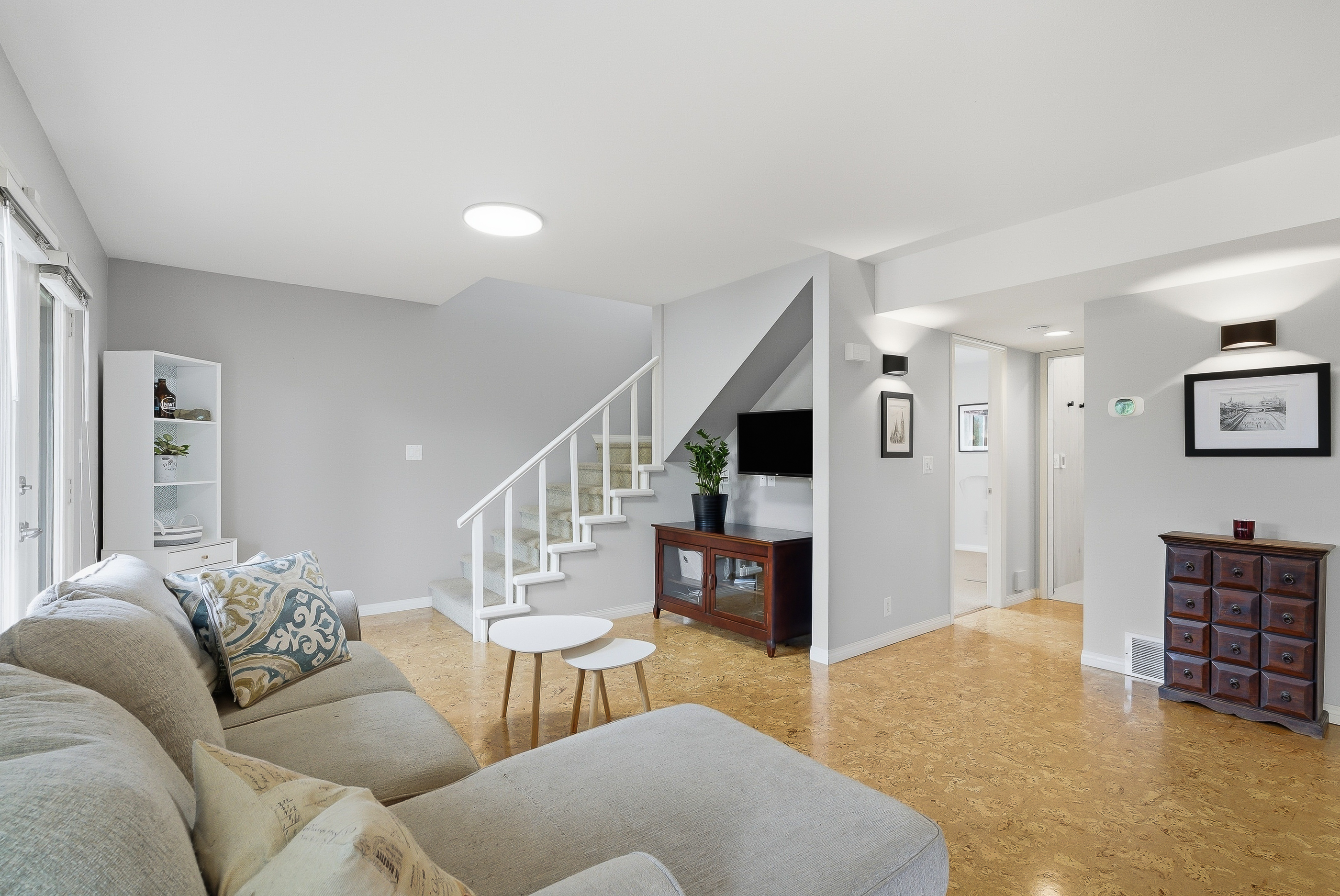 Open living room at 1127 Columbia St with cork flooring, white walls, staircase up to the bedrooms and natural light flooding in from the back