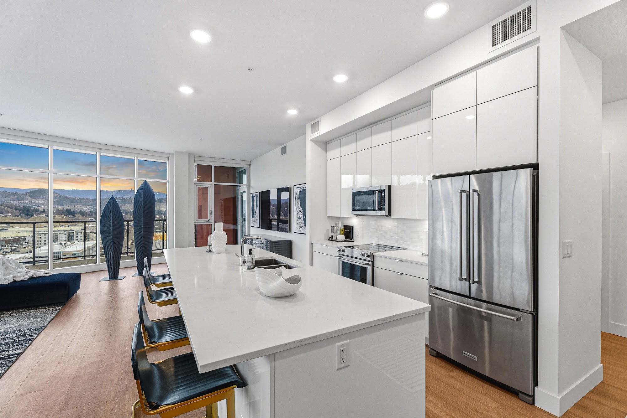 Open kitchen with white island, gold-leg bar stools, and the wrap-around window line behind