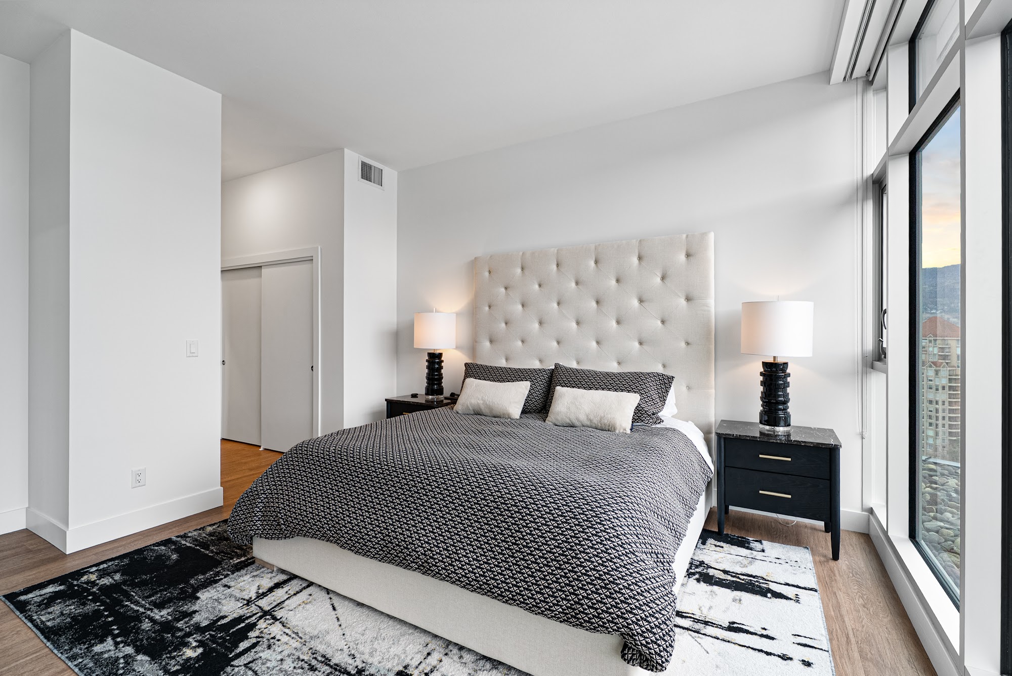 Primary bedroom with tufted ivory headboard and the city view through floor-to-ceiling glass