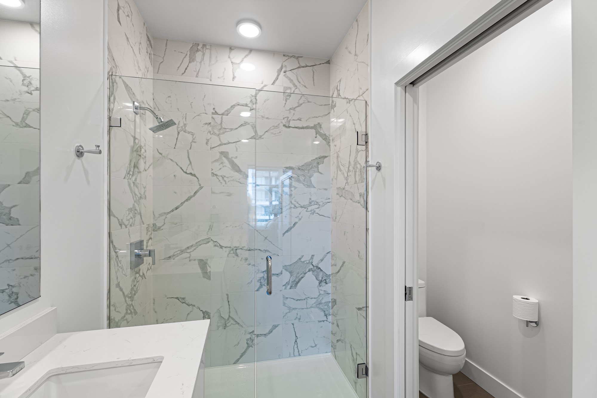 Primary ensuite with full-height marble shower surround and quartz double vanity